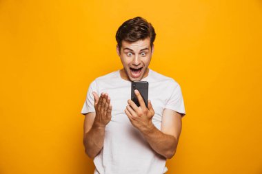 Cep telefonu sarı arka plan üzerinde izole bakarak mutlu bir genç adam portresi kutluyor