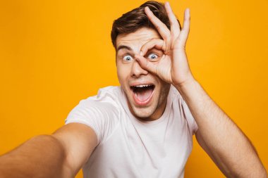 Bir selfie outsretched el ile alarak mutlu bir genç adam portresi, ok gösterilen sarı arka plan üzerinde izole