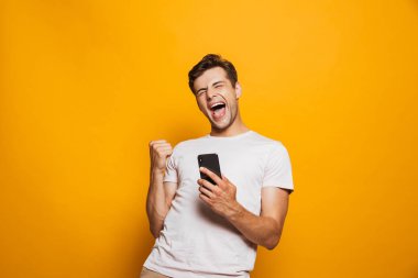 Sarı arka planda izole edilmiş cep telefonu tutan neşeli bir gencin portresi.