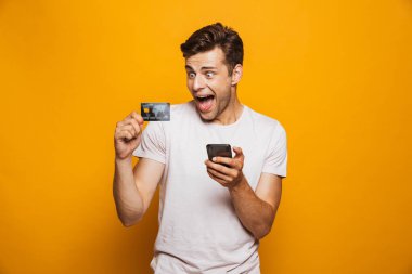 Hareket eden telefon tutarak ve kredi kartı izole sarı arka plan üzerinde gösterilen neşeli bir genç adam portresi