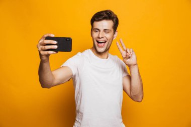 Sarı arka plan üzerinde izole bir selfie alarak mutlu bir genç adam portresi