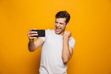 Başarı kutluyor sarı arka plan üzerinde izole bir selfie alarak mutlu bir genç adam portresi