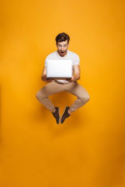 Tam uzunlukta sarı arka plan üzerinde izole dizüstü bilgisayar ile atlama şok bir genç adam portresi