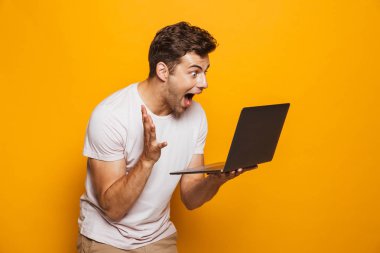 Sarı arka plan üzerinde izole dizüstü bilgisayar kullanan genç neşeli bir adam portresi