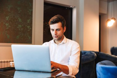 Kendine güvenen genç resmi giyimli adam otel lobisinde otururken dizüstü bilgisayar üzerinde çalışan