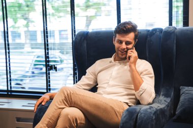 Otel lobisinde otururken cep telefonda konuşurken bir gülümseyen genç resmi giyimli adam portresi