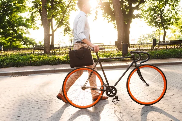 Genç bir adam bir bisiklet ile bir şehir sokak yürüyüş çanta ile gömlekli yan görünüm