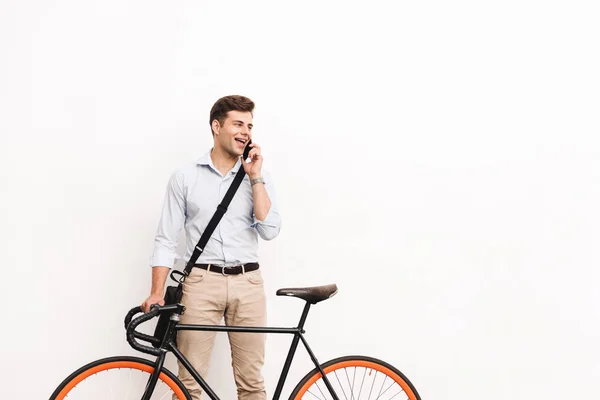 幸せな若い男の肖像を着たシャツ白い壁を越えて自転車で立ちながら携帯電話で話しています — ストック写真