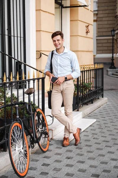 街で自転車とバッグの地位を運ぶシャツに身を包んだスタイリッシュなハンサムな若者の肖像 — ストック写真