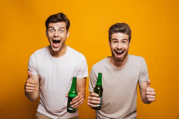 二人の興奮した若者の肖像親友黄色背景に分離を祝ってビール瓶と乾杯 — ストック写真