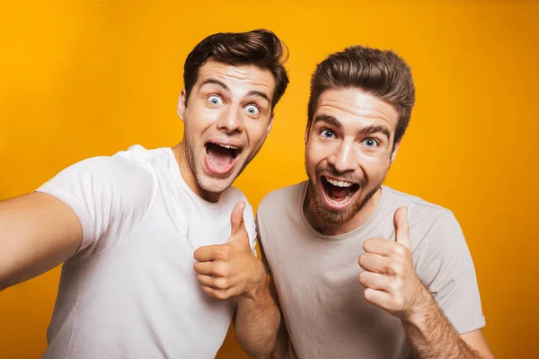 黄色の背景に分離された Selfie を取ることを親指を示す つ幸せな若い男性親友の肖像画 — ストック写真