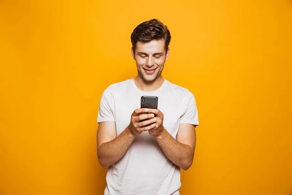 黄色の背景に分離された携帯電話を使用して幸せな若い男の肖像 — ストック写真