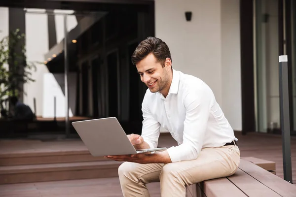 一个英俊的年轻的正式着装男子的肖像在笔记本电脑上工作 而坐在户外 — 图库照片