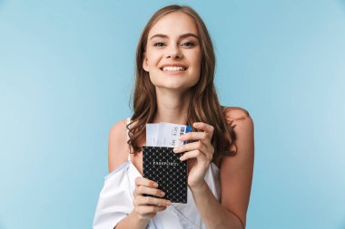 Yaz giysileri üzerinde mavi arka plan izole bilet uçan ile pasaport tutan güneş gözlüğü takıyor memnun bir genç kız portresi