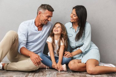 Mutlu bir aile baba, Anne, küçük kızı ise birlikte oturan ve gri arka plan üzerinde izole birbirlerine bakarak sarılma portresi