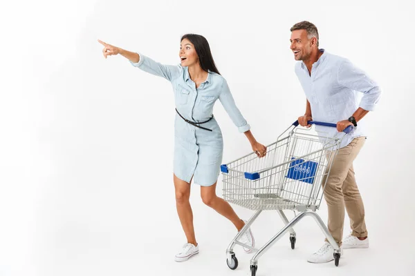 Casal Alegre Correndo Com Carrinho Compras Supermercado Apontando Para Longe — Fotografia de Stock