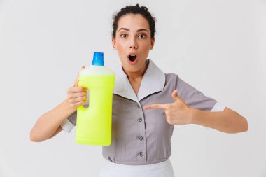 Beyaz arka plan üzerinde izole deterjan tutan üniformalı bir şok genç hizmetçi portresi giyinmiş