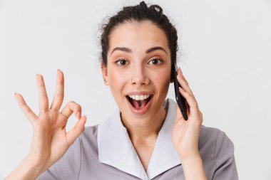 Neşeli bir genç hizmetçi portresi giyinmiş Tekdüzen gösteren beyaz arka plan üzerinde izole cep telefonunda konuşurken Tamam