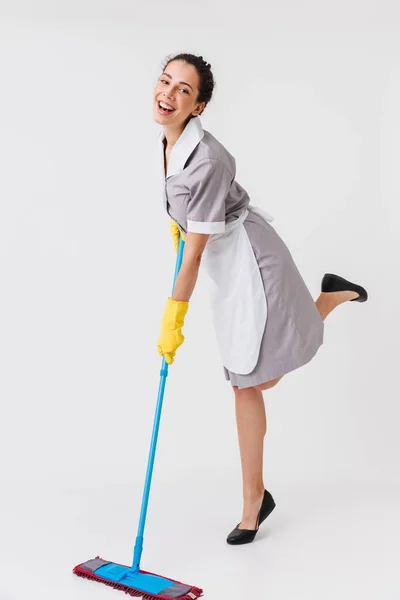 白い背景に分離したモップを使用して制服を着て陽気な若いメイドの完全な長さの肖像画 — ストック写真