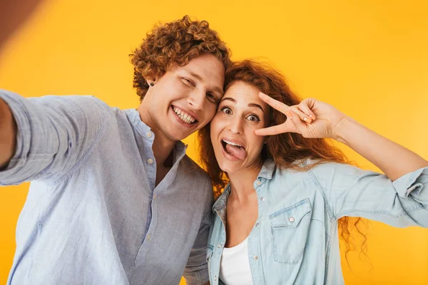 コンテンツのカップル男女黄色背景に分離した笑顔でピースサインを見せながら Selfie 写真を撮るのイメージ — ストック写真