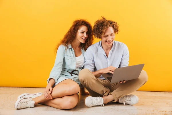 照片的年轻内容夫妇男女20S 坐在地板上 用银色笔记本电脑隔离的黄色背景 — 图库照片