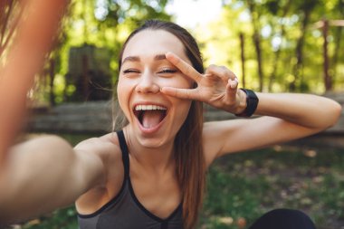 Açık havada otururken bir selfie alarak bir neşeli genç fitness kız portresi