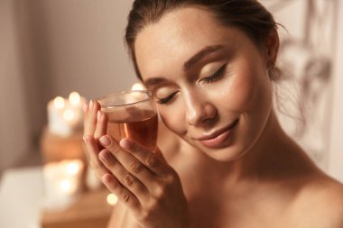 Spa merkezinde bir bardak bitki çayı tutan bir havlu sarılı oldukça genç bir kadın portresi kapatın