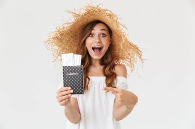 Mutlu güzel kadın 20'li yaşlarda giyen büyük hasır şapka beyaz arka plan üzerinde izole bilet pasaport tutarken sevindirici fotoğrafı