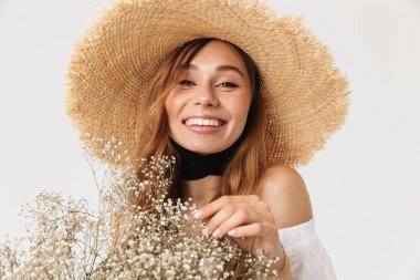 Mutlu gülümseyerek bakıyorsun ve beyaz arka plan üzerinde izole alan çiçek holding neşeli esmer kadın 20'li yaşlarda giyen büyük hasır şapka portresi