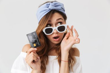 Görüntü bir yana ve beyaz arka plan üzerinde izole gösteren kredi kartı arıyorum heyecanlı zarif kadın 20'li yaşlarda giyen güneş gözlüğü