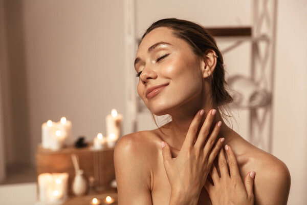 Portrait of a lovely young woman wrapped in a towel applying body cream at the spa center