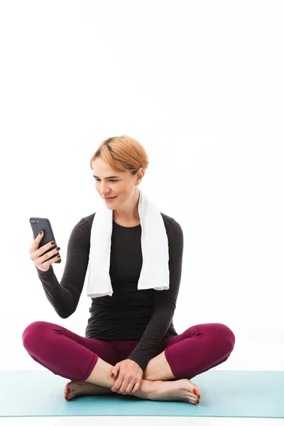 穿着运动衣的微笑女人的肖像坐在一个健身垫上 手机上的白色背景 — 图库照片