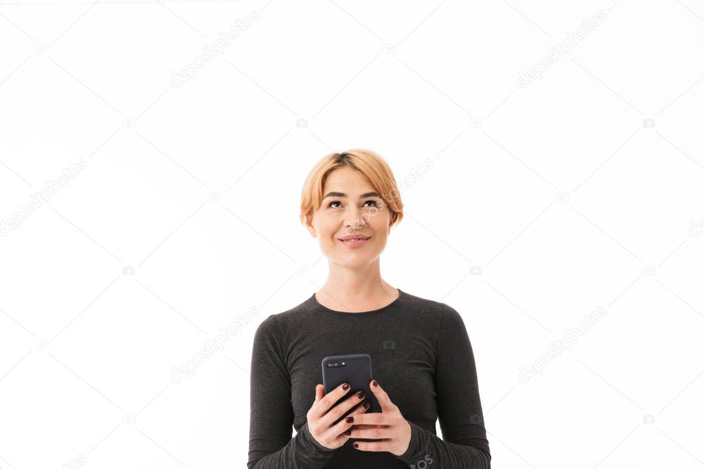 Portrait of a smiling yoga woman dressed in sport clothes using mobile phone and looking up over white background
