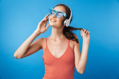 Güneş gözlüğü takıyor ve mavi arka plan üzerinde izole kulaklık ile müzik mayo memnun bir genç kız portresi