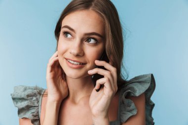 Mutlu genç kadın bir kenara cep telefonuyla konuşmak mavi arka plan bakmaktan izole duran resim.