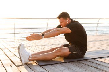 Müzik dinlerken spor halı üzerinde alıştırmalar yapmak imge-in yakışıklı genç sporcu açık havada sahilde.