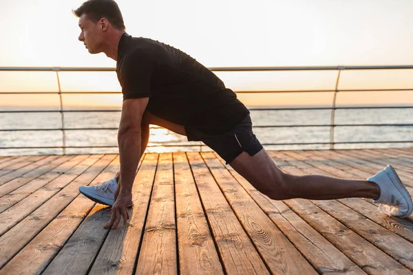 海辺で脚ストレッチをやって健康な若いスポーツマン — ストック写真