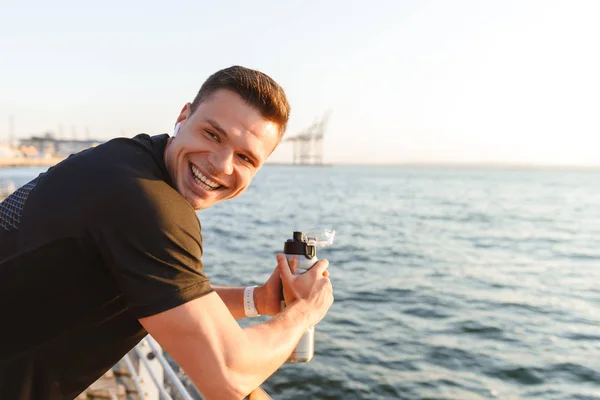 Happy Young Sportsman Earphones Holding Water Bottle While Leaning Rails — Stock Photo, Image