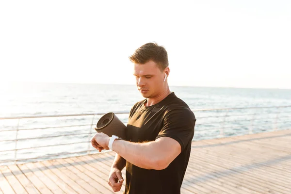 Joven Deportista Con Auriculares Mirando Reloj Mientras Está Pie Playa — Foto de Stock