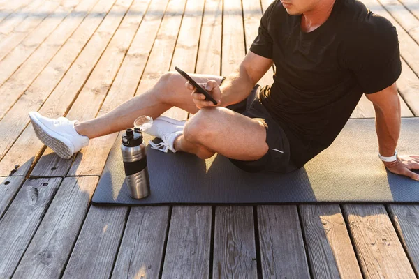 携帯電話を用いたスポーツ カーペットの上ビーチの屋外のハンサムな若いスポーツマンの写真をトリミング — ストック写真