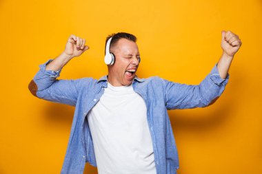 Sarı arka plan kulaklık ile müzik dinleme üzerinde izole heyecanlı duygusal adam görüntüsünü.