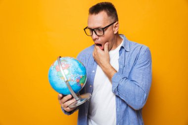 Şok adamın izole küre tutan sarı arka plan üzerinde fotoğraf.