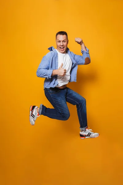 Image of emotional happy man jumping isolated over yellow background make thumbs up gesture.