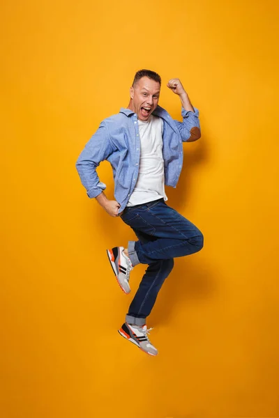 Image of emotional happy man jumping isolated over yellow background make winner gesture.