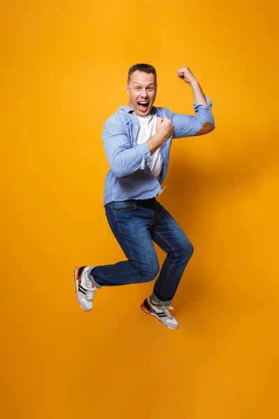 Image of emotional happy man jumping isolated over yellow background make winner gesture.