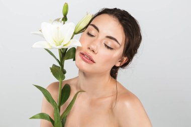 Genç ve güzel bir üstsüz kadın makyajlı yüzü gri arka plan üzerinde izole lily çiçek ile poz Güzellik Portresi