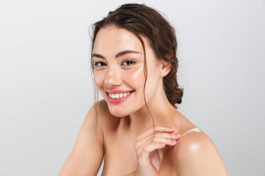 Gri arka plan üzerinde makyaj uygulayarak vücut kremi ile memnun genç bir üstsüz kadın portresi güzellik izole