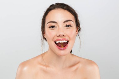Genç, neşeli bir üstsüz kadın ağzına gri arka plan üzerinde izole bir hap gösterilen makyajlı Güzellik Portresi