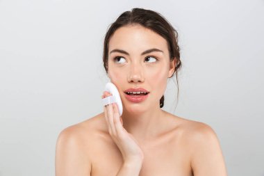 Gri arka plan üzerinde izole makyaj aplikatör ile çekici bir genç üstsüz kadın güzellik portresi