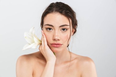 Genç ve güzel bir üstsüz kadın makyajlı yüzü gri arka plan üzerinde izole lily çiçek ile poz Güzellik Portresi